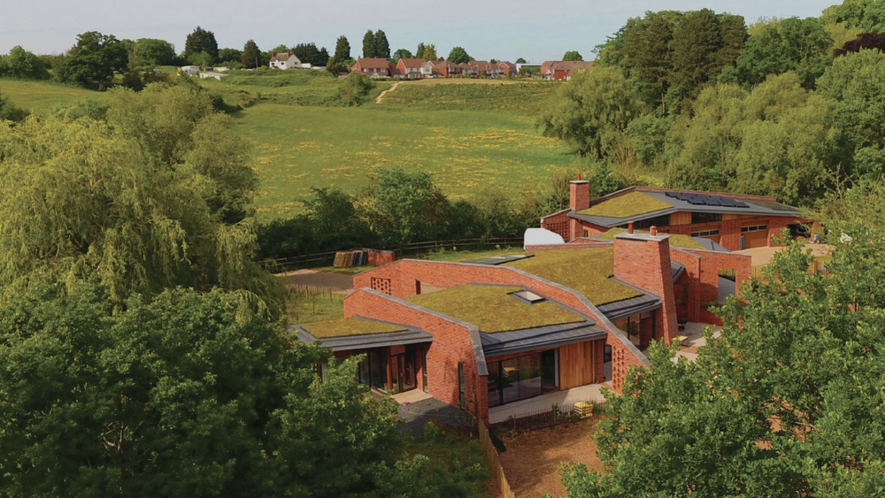 Modern brick house with green roof surrounded by trees and fields