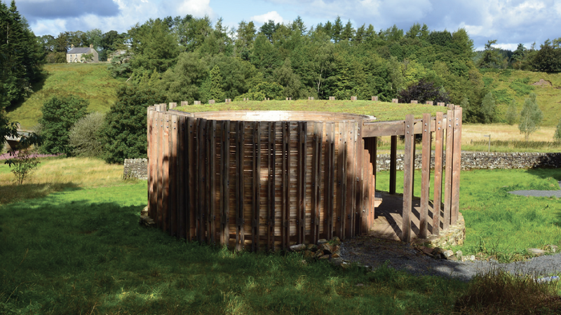 Wooden structure on a grassy area with trees and a house in the background