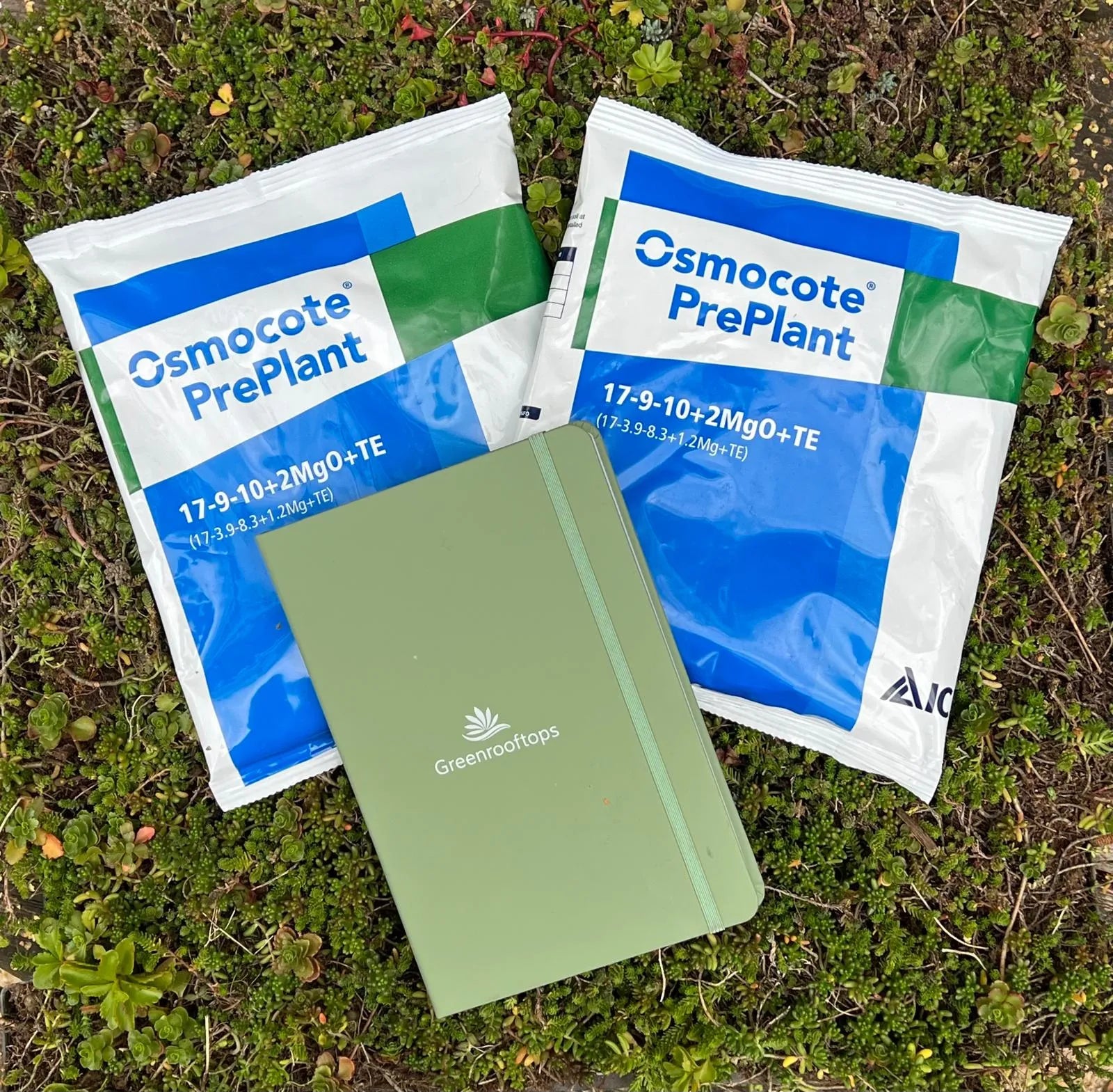 Two Osmocote PrePlant fertilizer packets and a Greenhops notebook on grass.